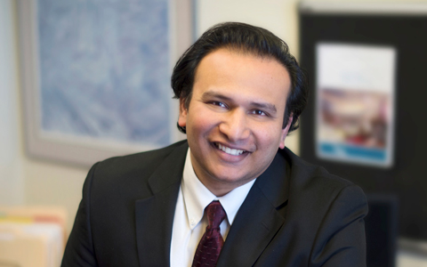 Amir Rizavi wearing a dark suit, yellow shirt and burgundy tie