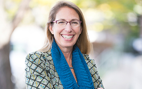 Headshot of Carol Lurie outside with her arms folded, wearing a blue scarf