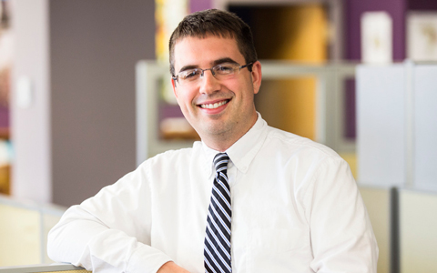 Mark Costa in the office wearing a white button-down shirt and striped tie