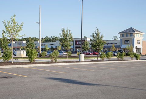 A parking lot sits in front of a row of shops.