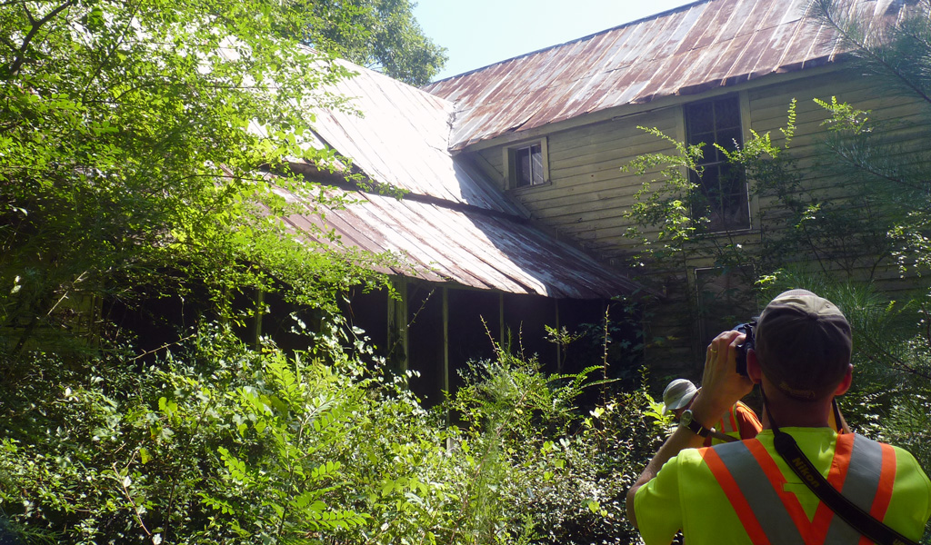 Person photographing historic home in wooded area