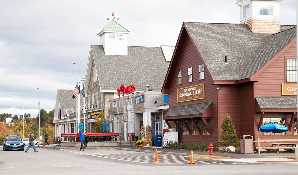 People walk past flagpoles at the building entrance of the Hooksett welcome center.