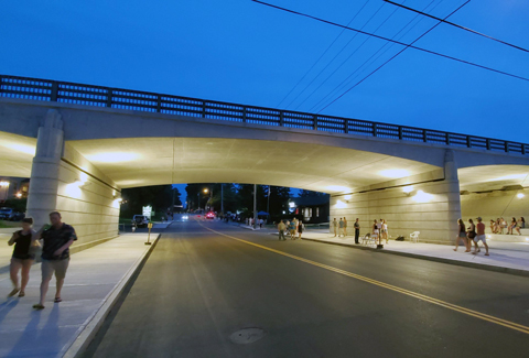 People walk under the newly reconstructed Main Street Bridge at twilight