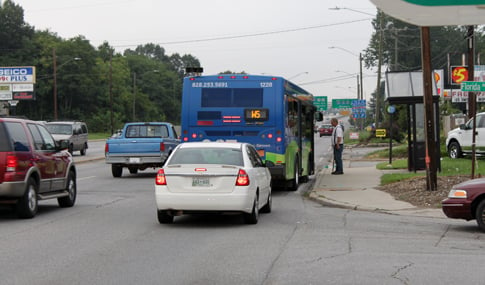 A man gets on a bus while a car is stopped behind it