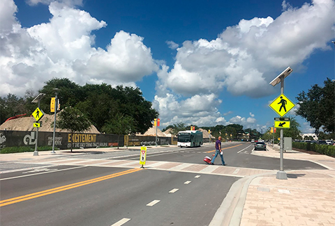 Man in the middle of a street crosswalk, with yellow signs and an oncoming bus in the other lane. 