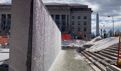 Water streams down a wall into a reflecting pool during the day