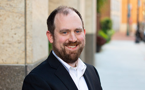 Mike Lowder poses in front of building wearing a black jacket.