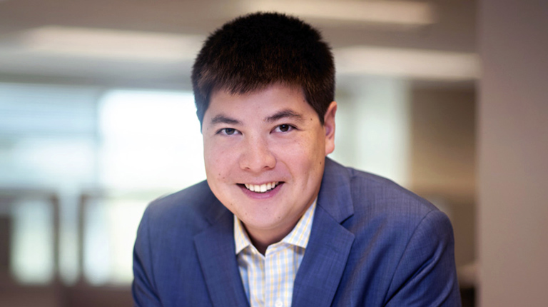 Andrew Nee leaning on a table at VHB while wearing a blue blazer. 