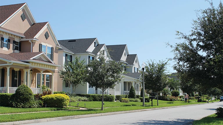 A view of a suburban street with new two-story houses and recently planted trees in the yards