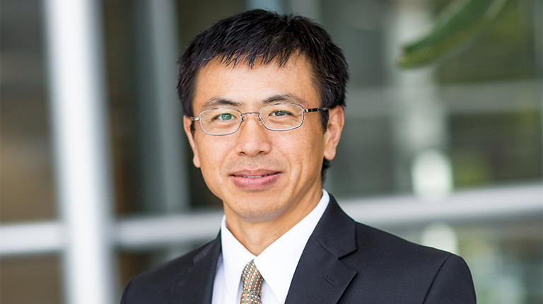 Baohong Wan standing outside wearing a black sports coat and tie.