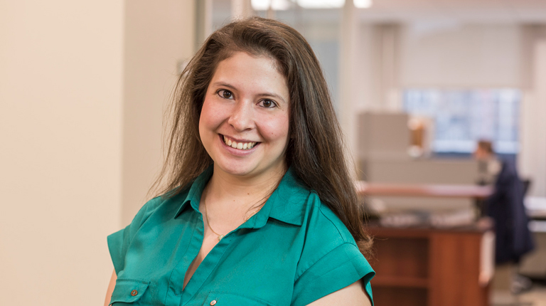 Elizabeth Jule wearing a teal shirt with the office in the background.