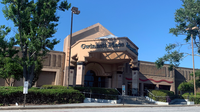 The entrance to a suburban shopping mall bordered by two trees and vegetative plantings. 