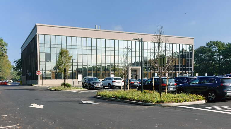  Parking lot with trees and a windowed building against a blue sky.