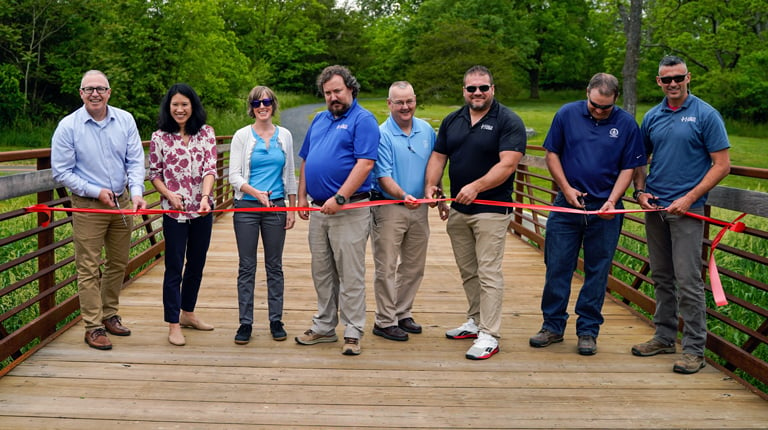 Eight individuals stand together to cut a red ribbon during the grand opening of the Friendly City Trail