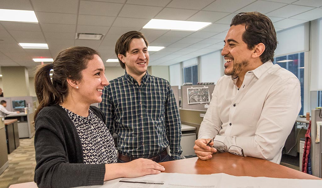 Three VHB employees collaborate during a meeting while reviewing plans.