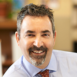 Ken Schwartz smiling in a light blue shirt and red tie.