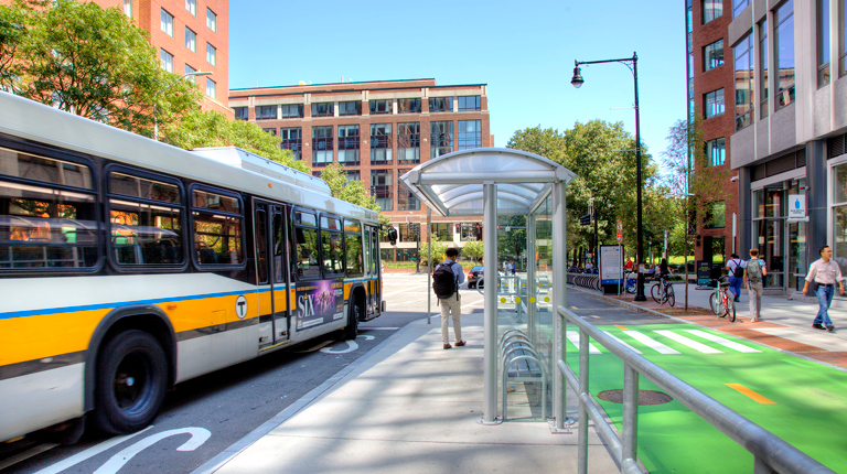 A bus drops off a passenger while bicyclists pedestrians use designated travel lanes and sidewalks.