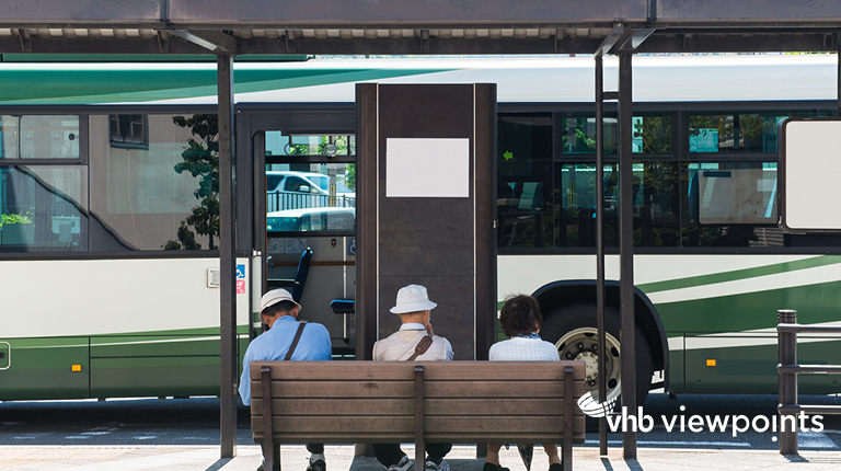 Transit riders wait on a bench as a bus approaches the bus stop.