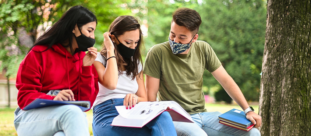 Three college students wear masks while looking at a textbook.