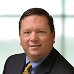 John Stronach in the office wearing a dark suit and tie. 