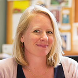  Sue Moberg in the office, wearing a blue shirt and beige cardigan.